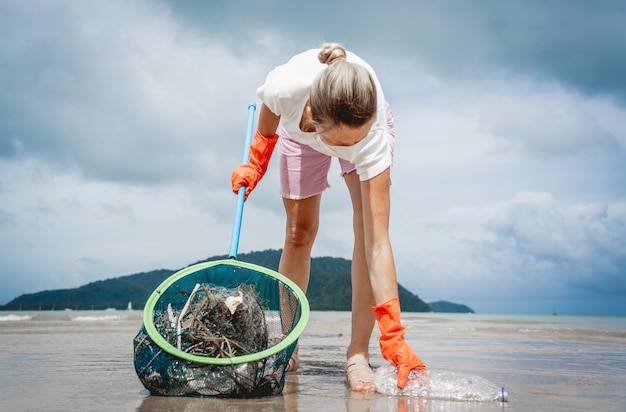 Wolontariuszka-ekolożka czyści plażę nad brzegiem morza z plastiku i innych odpadów