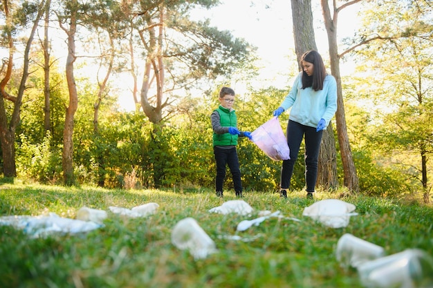 Wolontariuszka i mały chłopiec zbierają plastikowe śmieci i wkładają je do biodegradowalnego worka na śmieci na zewnątrz. Koncepcja ekologii, recyklingu i ochrony przyrody. Ochrona środowiska.