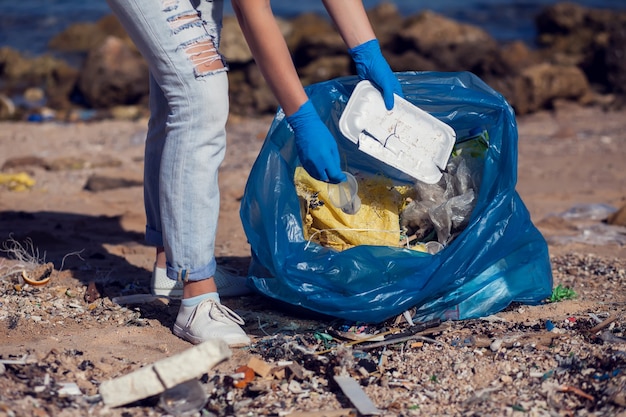Wolontariuszka w białej koszulce z dużą niebieską torbą na śmieci na plaży. Koncepcja zanieczyszczenia środowiska
