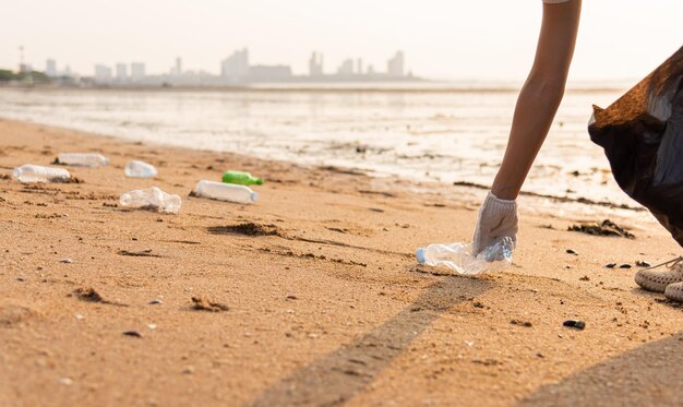 Wolontariuszka wkładająca plastikową butelkę do czarnej plastikowej torby na śmieci do czyszczenia plaży