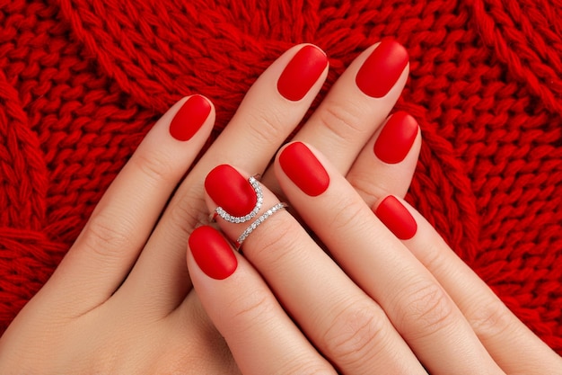 Womans ręce z matowym manicure na czerwonej dzianinowej kołdrze zimowy manicure pedicure trendy w projektowaniu