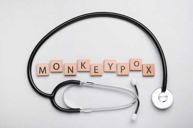 Word Monkeypox wykonany z drewnianych kostek i stetoskopu na jasnym tle leżał płasko