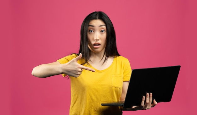 Wow koncepcja oferty Portret wstrząśniętej chińskiej damy trzymającej komputer przenośny i wskazującej na to różowe tło