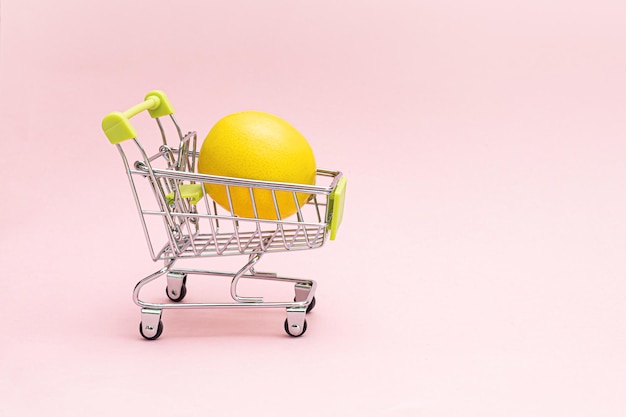 Wózek na zakupy z cytryną na różowym tle Koncepcja sklepu spożywczego i spożywczego