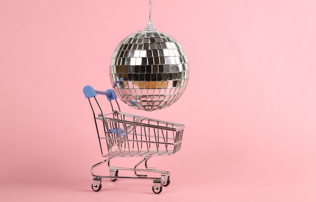 Wózek na zakupy z kulą dyskotekową na różowym tle Koncepcja partii minimalizmu