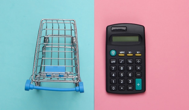 Zdjęcie wózek sklepowy z kalkulatorem w kolorze różowo-niebieskim. kalkulacja ekonomiczna zakupów, koszty zakupu.
