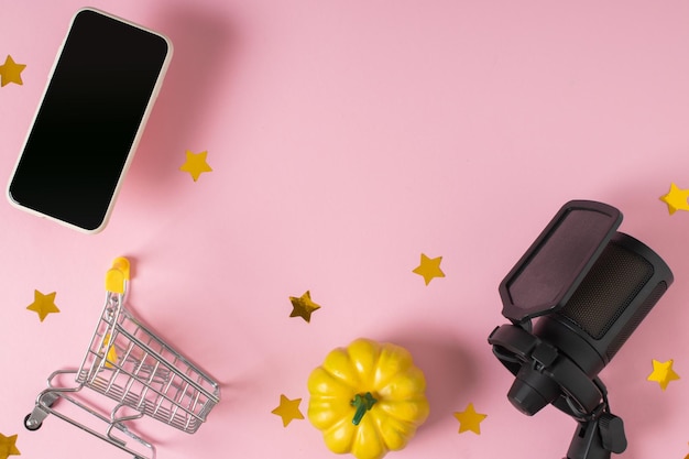 Wózek w supermarkecie ze smartfonem z mikrofonem i dynia na różowym tle Sprzedaż i sklepy internetowe na święta Halloween