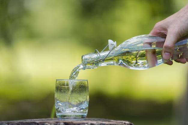 Wręcza Dolewanie Pije Wodę Od Butelki W Szkło Z Naturalnym Tłem