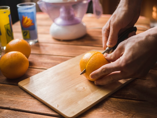 Wręcza tnące świeże pomarańcze z nożem na drewnianej powierzchni robić soku smoothie