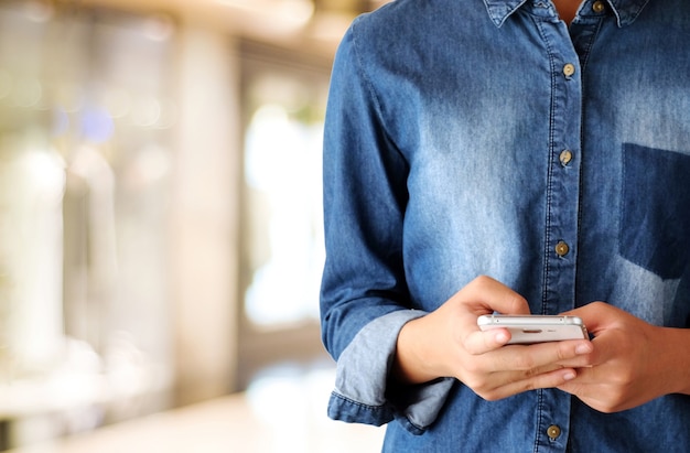 Wręcza używać mądrze telefon nad plama sklepem z bokeh światła tłem