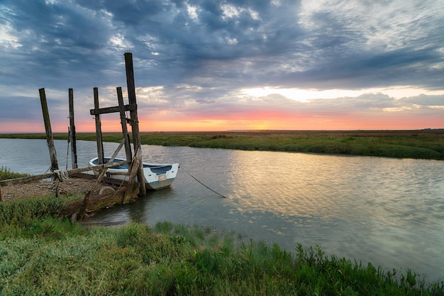 Wschód słońca nad łodzią zacumowaną do starego drewnianego molo w Thornham