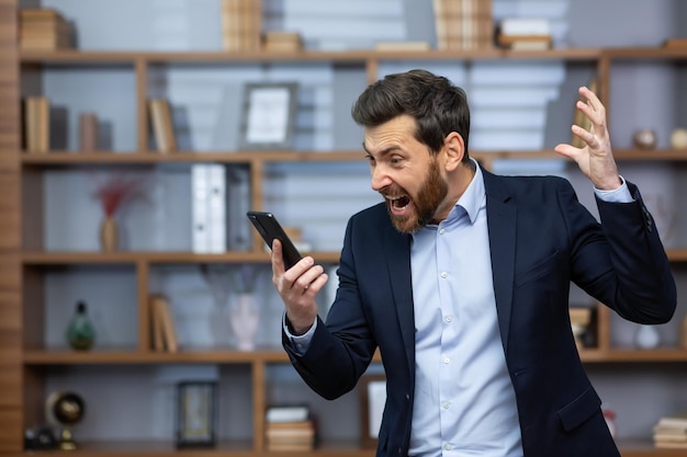 Wściekły szef kłócący się i krzyczący na telefon mężczyzna w garniturze w pracy w biurze