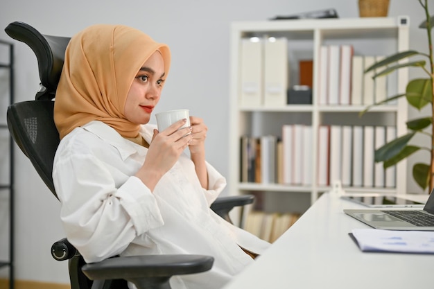 Wspaniała azjatycka muzułmańska bizneswoman popijająca kawę i marząca o sukcesie biznesowym
