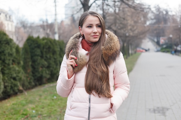 Wspaniała młoda kobieta z pięknymi oczami i brunetką, z naturalnym makijażem. Atrakcyjna młoda dama na ulicy miasta, odwraca się do aparatu i daje piękny figlarny uśmiech. futrzany kołnierz