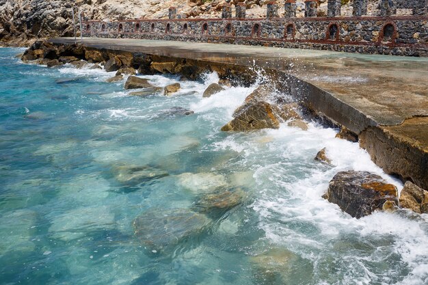 Wspaniałe widoki na błękitne Morze Śródziemne. Słoneczne skały, fale z pianą i bryzgającą wodą. Fala uderza w skały na brzegu