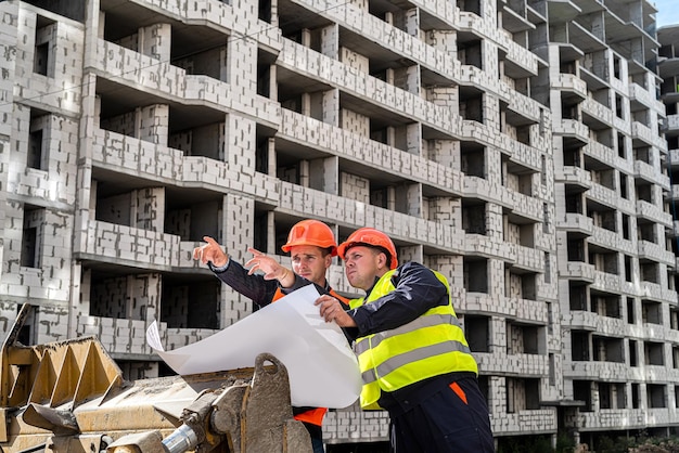 Wspaniali mężczyźni w mundurach i kaskach rozważają plan nowej budowy, umieszczając papier na równiarce Koncepcja budowy