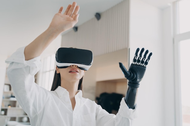 Współczesna niepełnosprawna dziewczyna w okularach VR wchodząca w interakcję z rozszerzoną rzeczywistością za pomocą bionicznej protezy ramienia