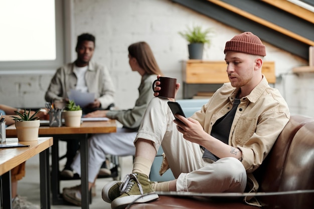 Współczesny biznesmen w codziennym stroju pijący kawę i piszący SMS-y podczas przerwy