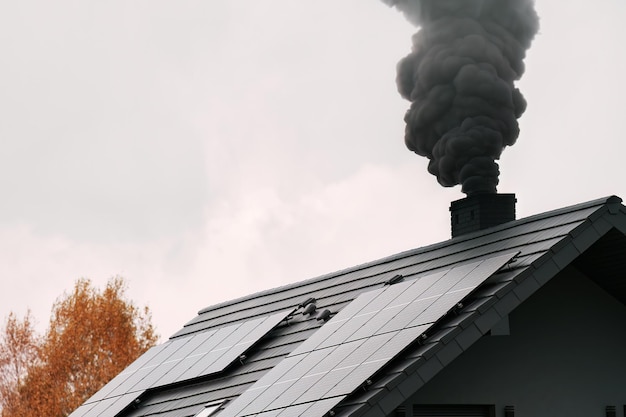 Współczesny dom emituje czarny dym z komina w zimie, co powoduje zanieczyszczenie środowiska i globalne ocieplenie Czarny dym ze komina domu na wsi pokazuje wpływ ogrzewania