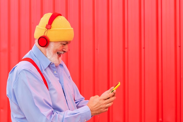 Współczesny emeryt słuchający muzyki przez słuchawki podczas wysyłania wiadomości na swoim telefonie komórkowym