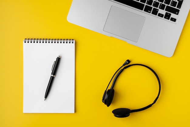 Współczesny obszar roboczy na żółtym tle notebooka z długopisowym laptopem i cyfrowym zestawem słuchawkowym