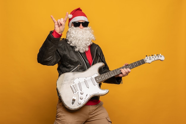 Współczesny Święty Mikołaj w skórzanej kurtce, rebel rock n roller grający na gitarze emocjonalnie odizolowany na żółtym tle