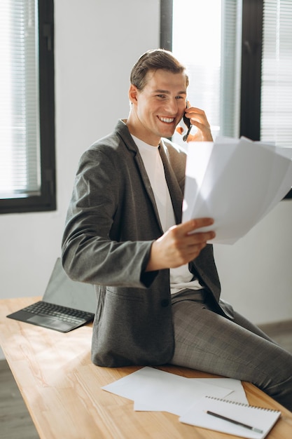 Współczesny uśmiechnięty pracownik biurowy trzymający dokumenty i rozmawiający przez telefon