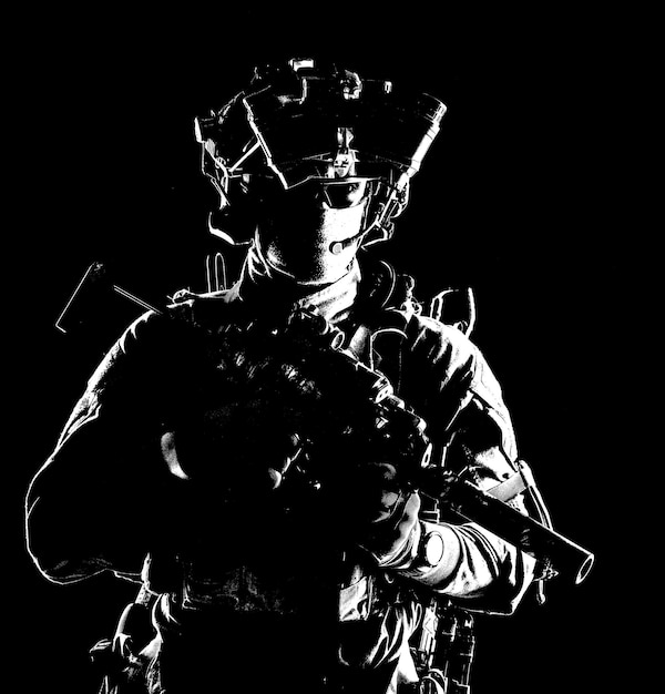 Współczesny żołnierz piechoty sił specjalnych, strzelec grupowy, uzbrojony pistolet maszynowy z tłumikiem wyposażony w zestaw słuchawkowy z radiem i quadtube noktowizor stojący w ciemnościach
