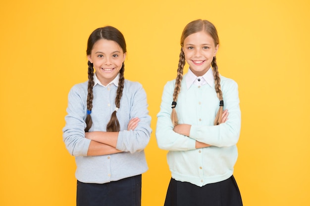 Wspólna nauka to fajna zabawa inteligentne małe dziewczynki na żółtym tle dzień wiedzy szczęśliwe dzieciństwo moda dziecięca koncepcja edukacji przyjaźni i siostrzeństwa powrót do szkoły dziewczyny w mundurkach szkolnych