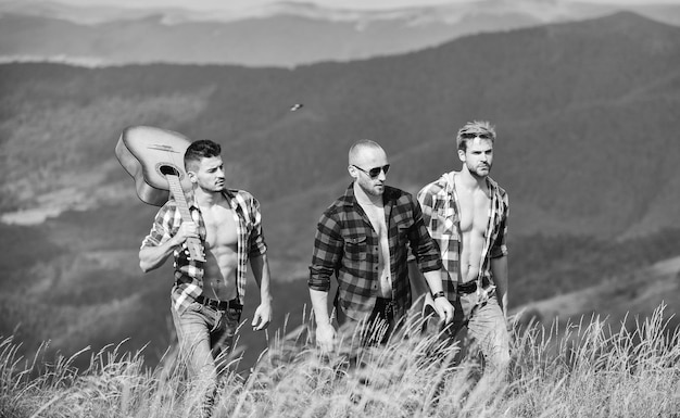 Wspólna radość z wolności Grupa młodych ludzi w kraciastych koszulach spacerujących razem po szczycie góry Mężczyźni z gitarą wędrująca w słoneczny dzień Koncepcja turystyki pieszej turystów Wędrówka z przyjaciółmi Długa trasa
