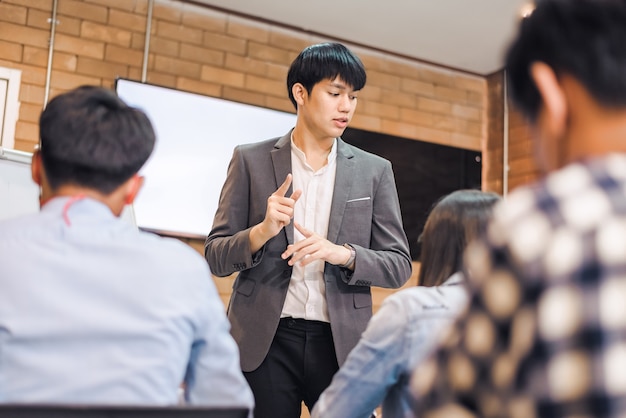 Współpraca biznesowa: Młody azjatycki trener płci męskiej lub mówca przedstawia prezentację flipchartu różnym przedsiębiorcom na spotkaniu w biurze. Nauczyciel lub trener przedstawia projekt różnym kolegom.
