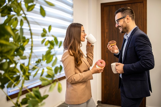 Zdjęcie współpracownicy biznesowi na przerwie w pracy rozmawiają i cieszą się kawą i pączkami
