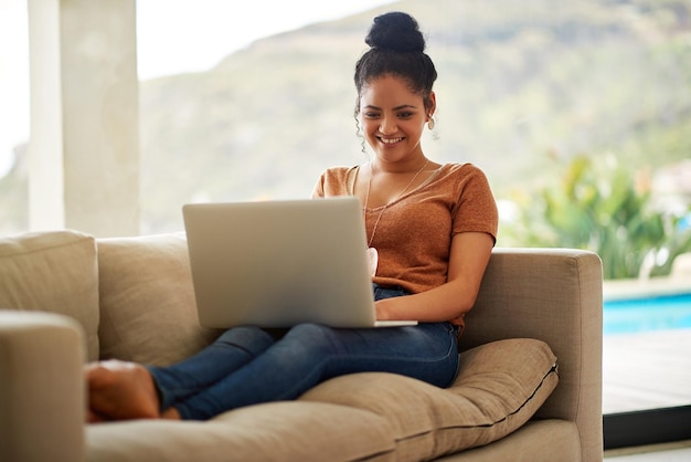Wszystkie te aktualizacje statusu w mediach społecznościowych są zbyt zabawne Ujęcie pięknej młodej kobiety siedzącej na kanapie przy laptopie w domu