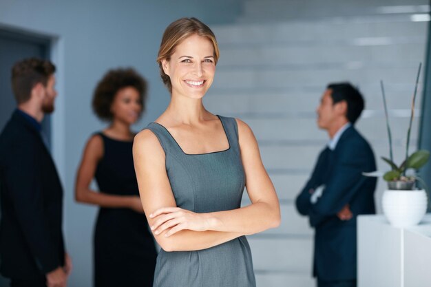 Wszystko jest możliwe z zaangażowanym zespołem za Tobą Portret młodej bizneswoman stojącej w biurze z kolegami w tle