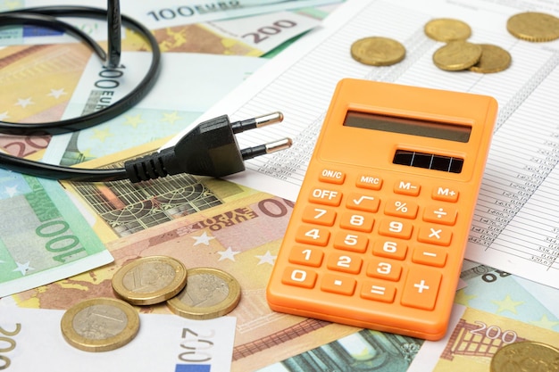 Wtyczka zasilania i kalkulator na tle banknotów euro Zwiększenie zużycia Koszt energii elektrycznej Koncepcja drogiej energii Podwyżka cen Ogrzewanie Kryzys Rachunek za usługi komunalne Oszczędzanie Konserwacja Inflacja