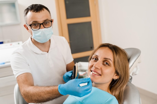 Wybielanie zębów Dentysta pracujący z kolorami zębów Pacjent patrzący w lustro Stomatologia Lekarz sprawdzający próbki koloru zębów w gabinecie stomatologicznym