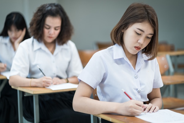 Wybiórcze skupienie nastoletnich studentów siedzi na krześle wykładowym, pisze na papierze egzaminacyjnym arkusz odpowiedzi, biorąc udział w egzaminie końcowym lub klasie. Studenci w mundurach w klasie.