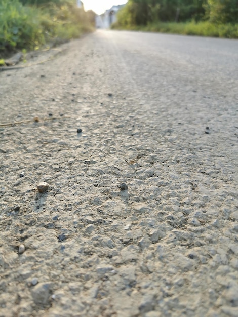 Wyboista betonowa droga z małym i dużym żwirem, prowadząca na wprost wieczorem wyboista droga