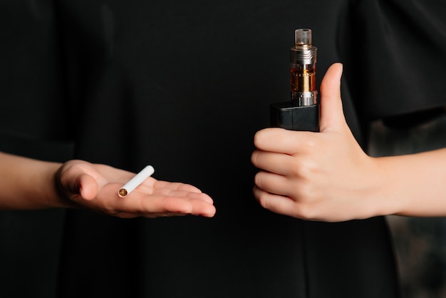 Wybór między papierosem tytoniowym a papierosem elektronicznym. Zakończenie żeńskie ręki. Kciuk w górę dla e-liquidu.