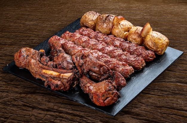 Wybór różnych grillowanych mięs dla smakoszy na czarnej desce z rustykalnym drewnianym tłem Szaszłyk z jagnięciny z ziemniakami kebab