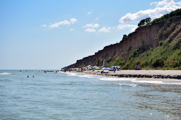 Wybrzeże nadmorskiej plaży z ludźmi odpoczywającymi na piaszczystym brzegu Nad plażą wisi klif