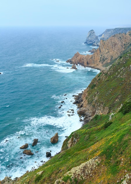 Wybrzeże Oceanu Atlantyckiego (granitowe głazy i klify morskie) przy pochmurnej pogodzie. Widok z Cape Roca (Cabo da Roca), Portugalia.