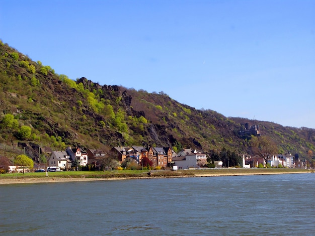 Zdjęcie wybrzeże renu, niemcy, szeroka szybka rzeka, wiele pięknych domów, zbocza górskie, błękitne niebo,