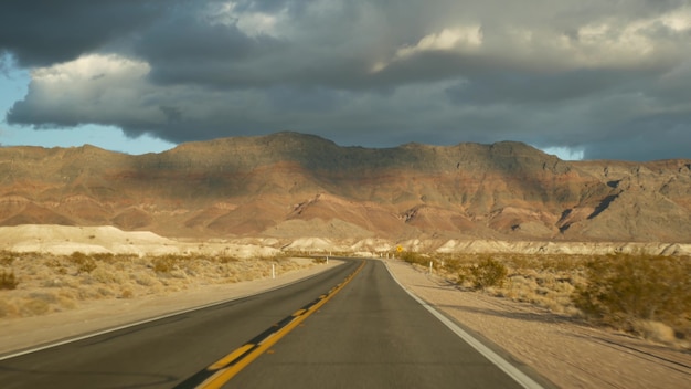 Wycieczka samochodowa z Doliny Śmierci do Las Vegas w stanie Nevada USA. Autostop podróżowanie po Ameryce. Podróż autostradą, dramatyczna atmosfera, góra o zachodzie słońca i pustynia Mojave. Widok z samochodu.