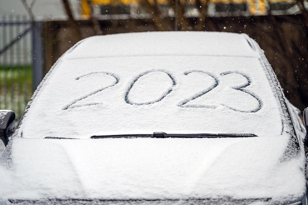 Wycieraczki przedniej szyby i pokryty śniegiem samochód 2023 napis odręcznie na śnieżnym oknie