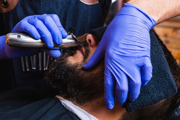 Wycięte z rąk fryzjera, który za pomocą golarki elektrycznej zabiera klientowi brodę