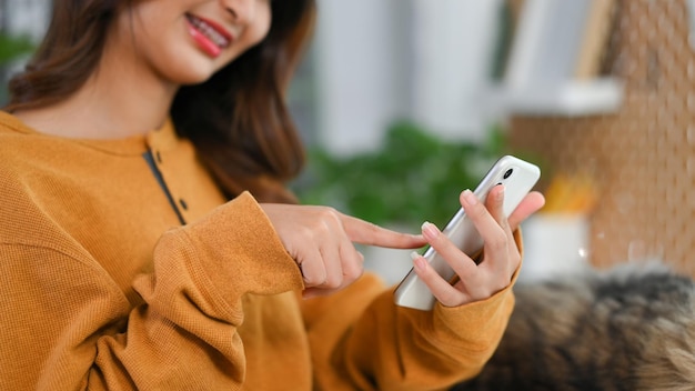 Wycięte zdjęcie uśmiechniętej młodej kobiety wysyłającej wiadomość na telefon komórkowy Ludzie i koncepcja technologii