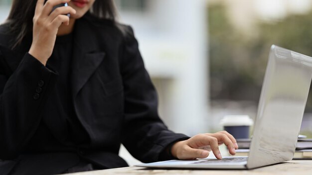 Wycięte zdjęcie zajętej bizneswoman rozmawiającej przez telefon komórkowy i sprawdzania informacji na laptopie