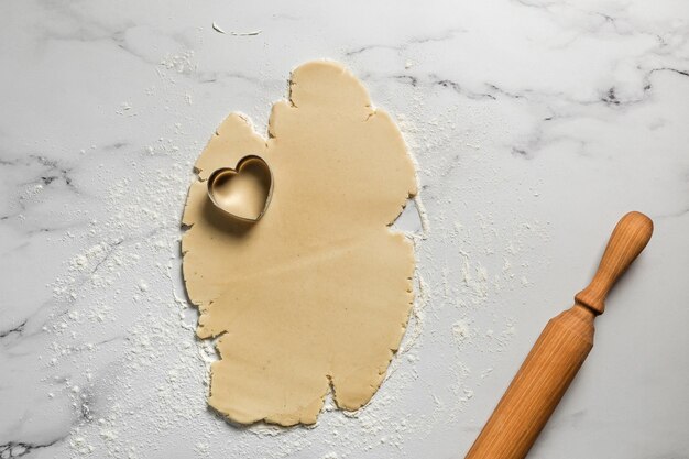Wycinanie ciasteczek w kształcie serca z rozwałkowanego ciasta kruchego na marmurowym stole posypanym mąką widok z góry na wałek do ciasta Pieczenie na walentynki