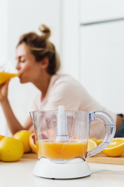 Wyciskarka do cytrusów i kobieta pijąca świeżo wyciśnięty sok z pomarańczy domowej roboty